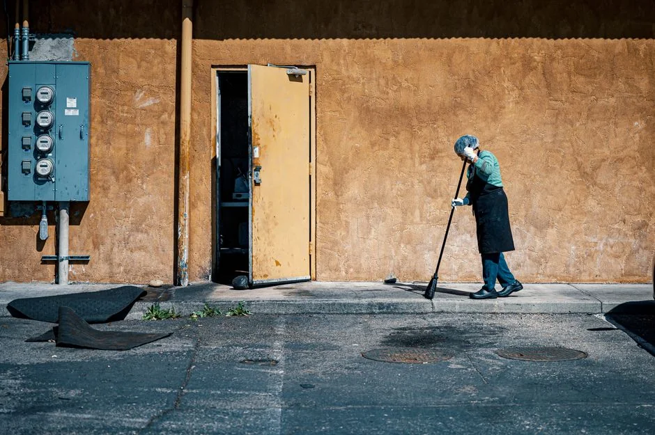 A man cleaning a glass barrier outdoors with a squeegee, surrounded by greenery.